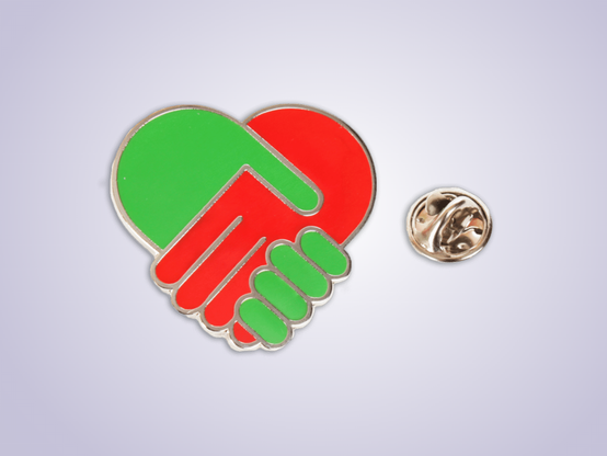 Speldje van GLPvdA waarbij 2 handen elkaar een hand geven. De bovenliggende hand heeft wel erg lange vingers (/korte handpalm)