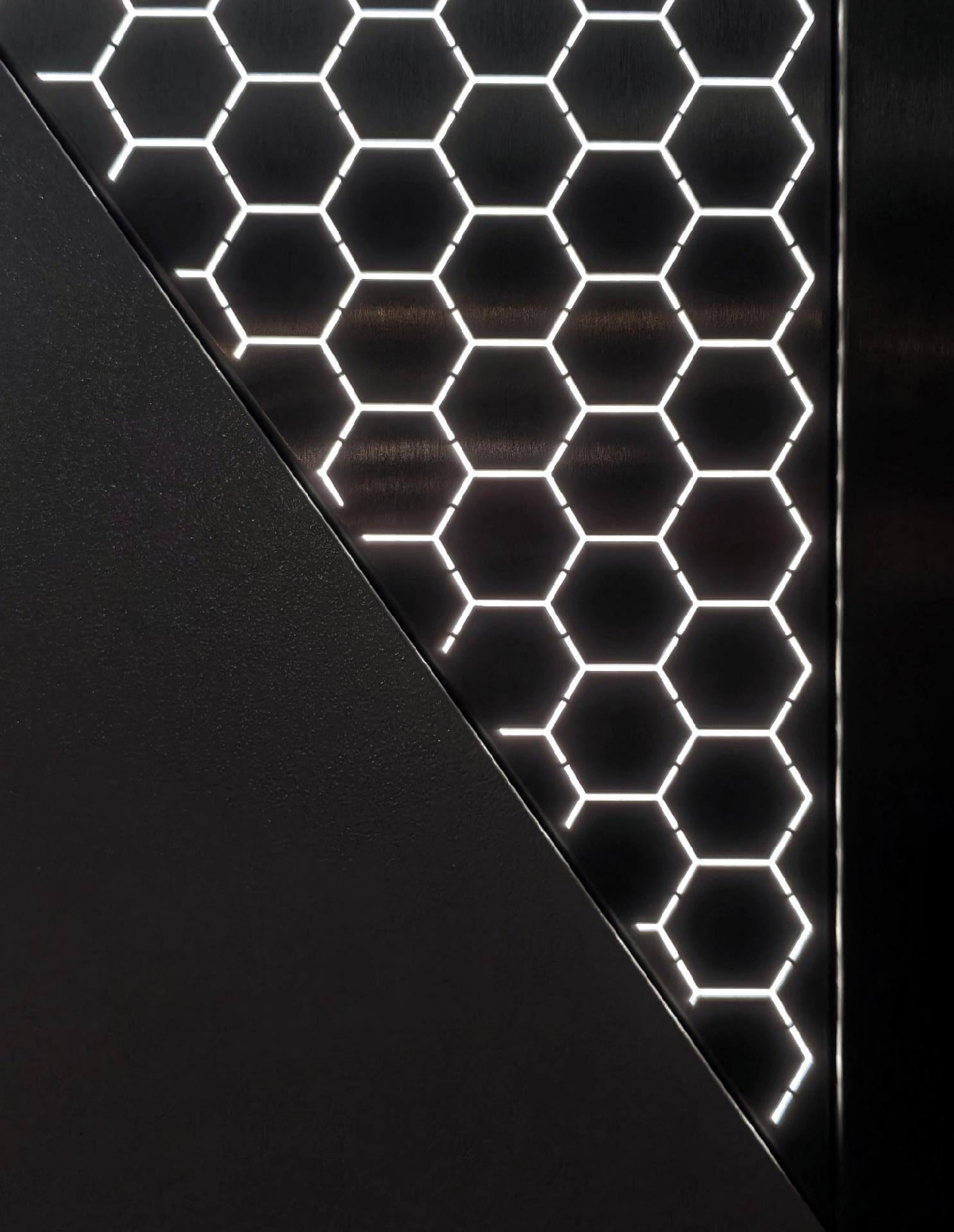 An almost black and white photo showing a pattern of illuminated hexagons that form a grid on a dark metallic surface divided diagonally by a solid black section.