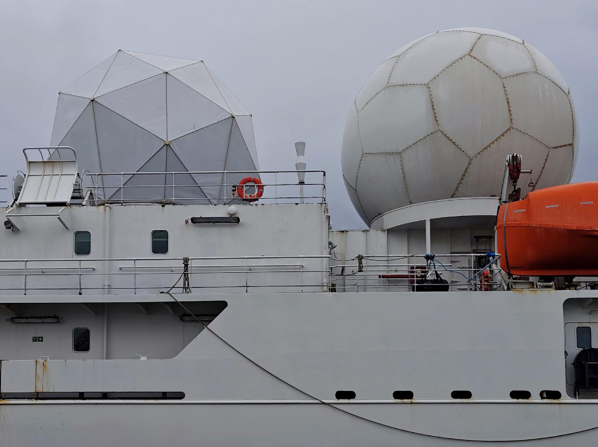 A photo showing a mostly white part of a large ship with two large radar done structures on its upper deck.