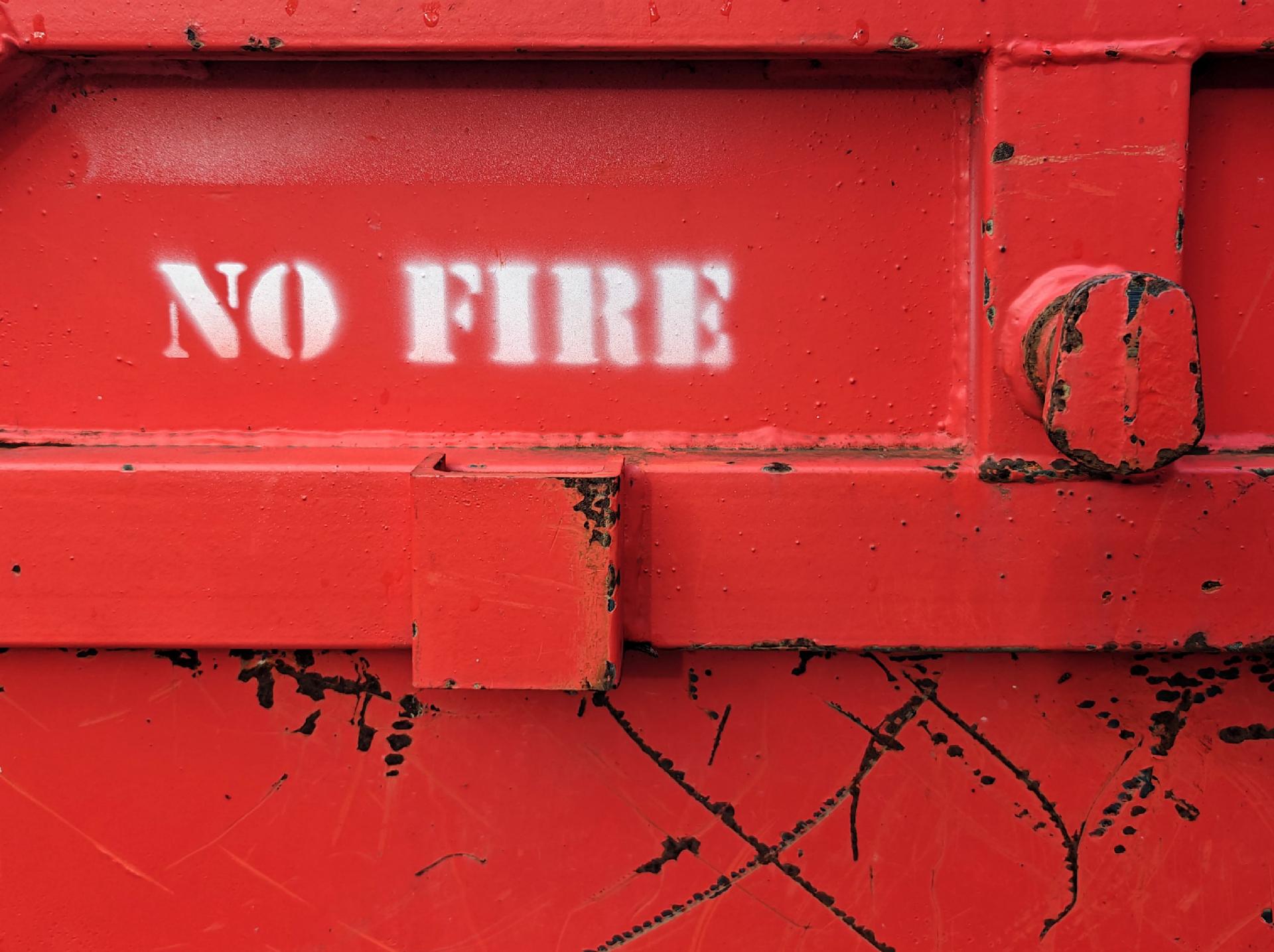 Close up foto of the side of a fire-red skip, with white stencilled words saying โNO FIREโ.