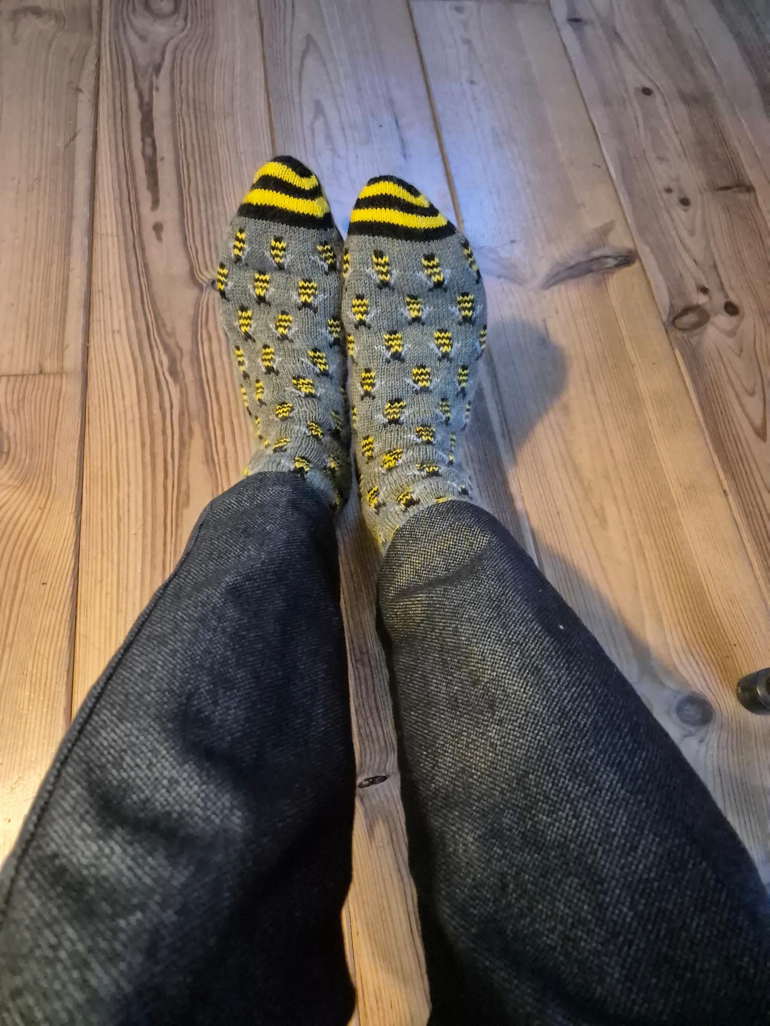 Two feet wearing hand knit green socks with bumble bees