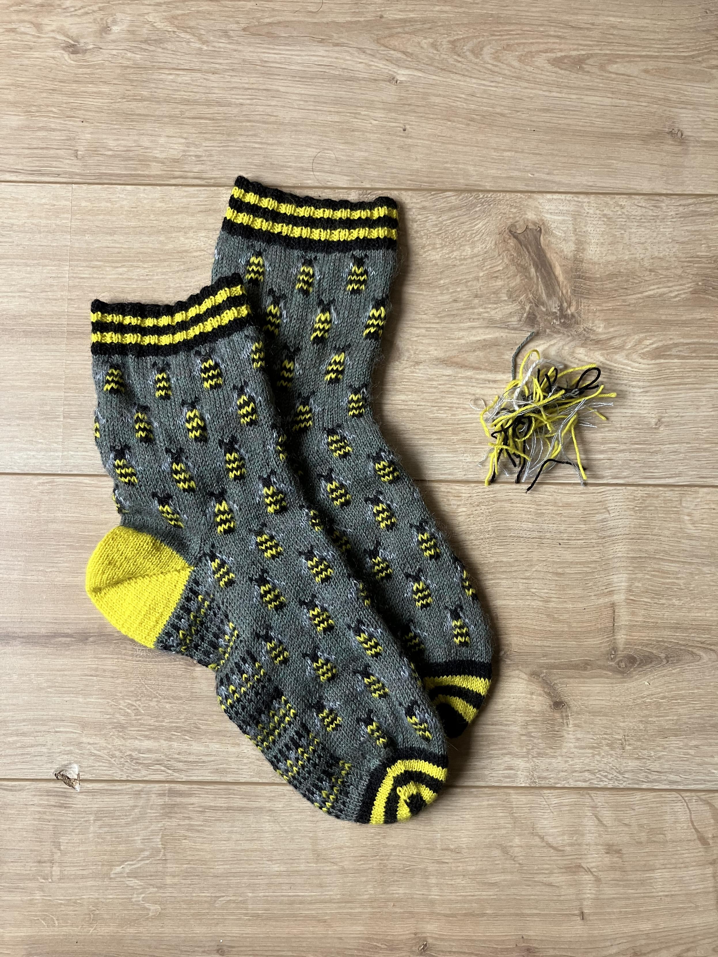 Green socks with bumblebees knitted in, posed flat on a wooden surface 