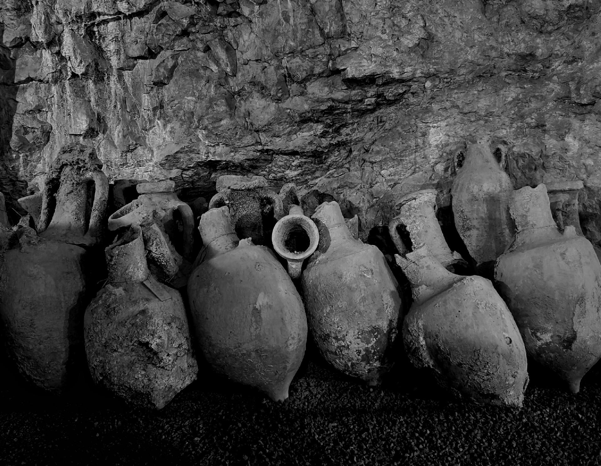 A black and white photo showing a jumble of ancient clay amphorae in a rocky cave.