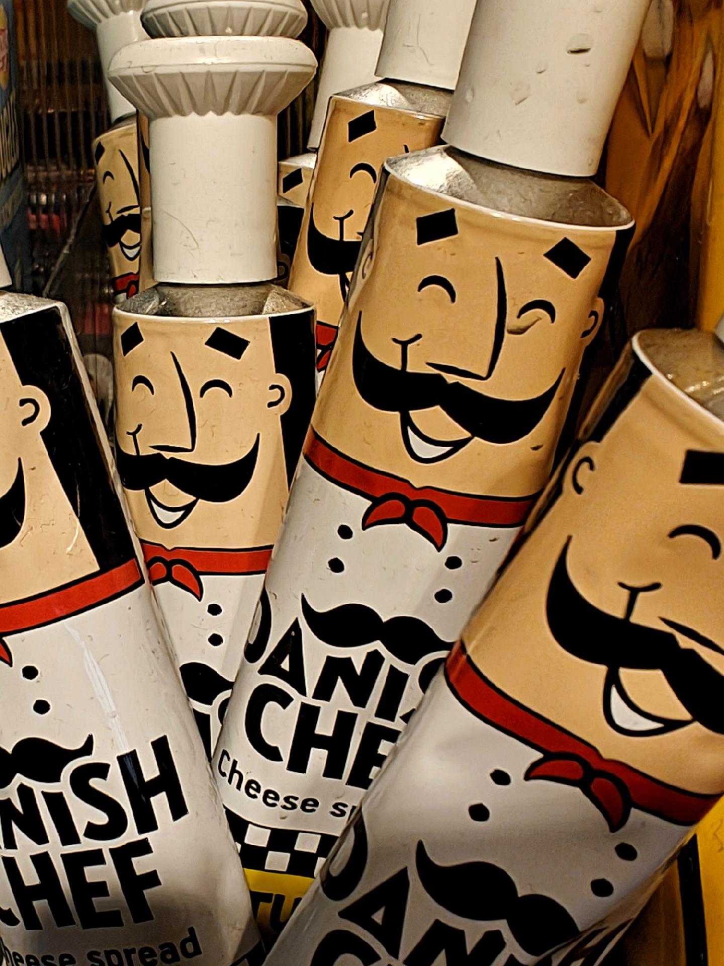A close up photo of a bunched up group of 'cheese spread' tubes featuring smiling chef faces, white tube caps in the shape of a cook's hat.