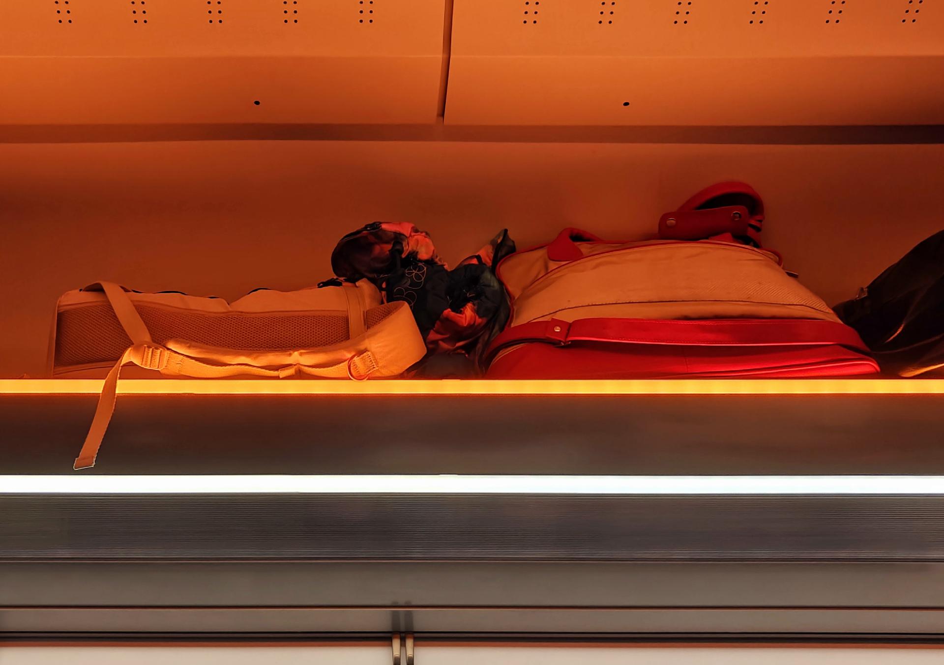 A photo showing several bags placed on a overhead shelf with warm orange lighting and a bright white line of light below.