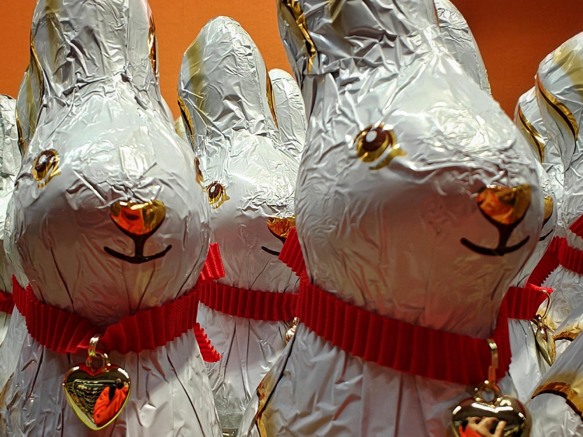 A close-up photo of white foil-wrapped chocolate bunnies with red ribbons and gold heart charms.