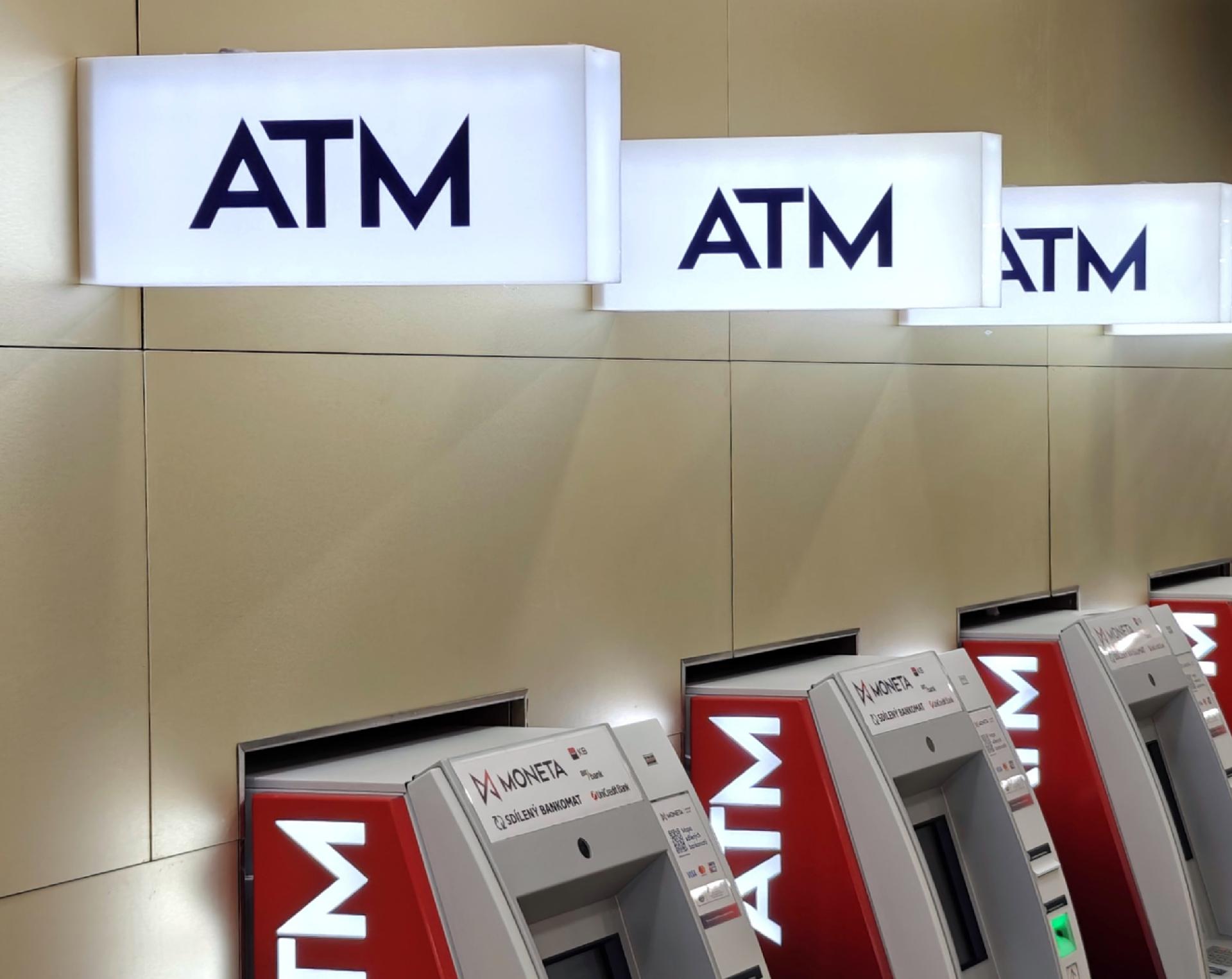 A photo showing parts of three ATM machines in a row with white illuminated "ATM" signs above them.