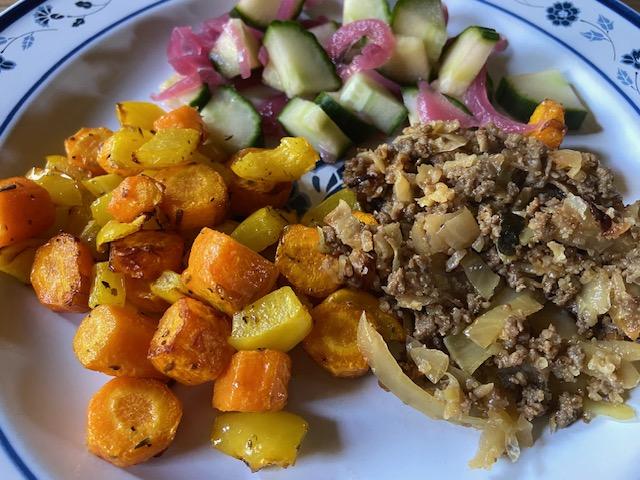 Bord met geroosterde wortel en gele paprika, een gehaktmengsel en komkommer met zure rode ui.