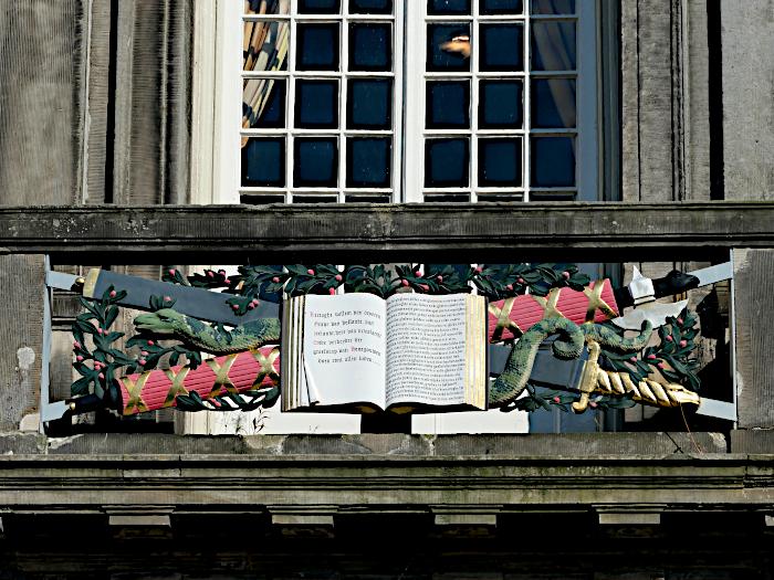 Foto van decoratie aan stadhuis van Enkhuizen met afbeelding van boek, slang en zwaard