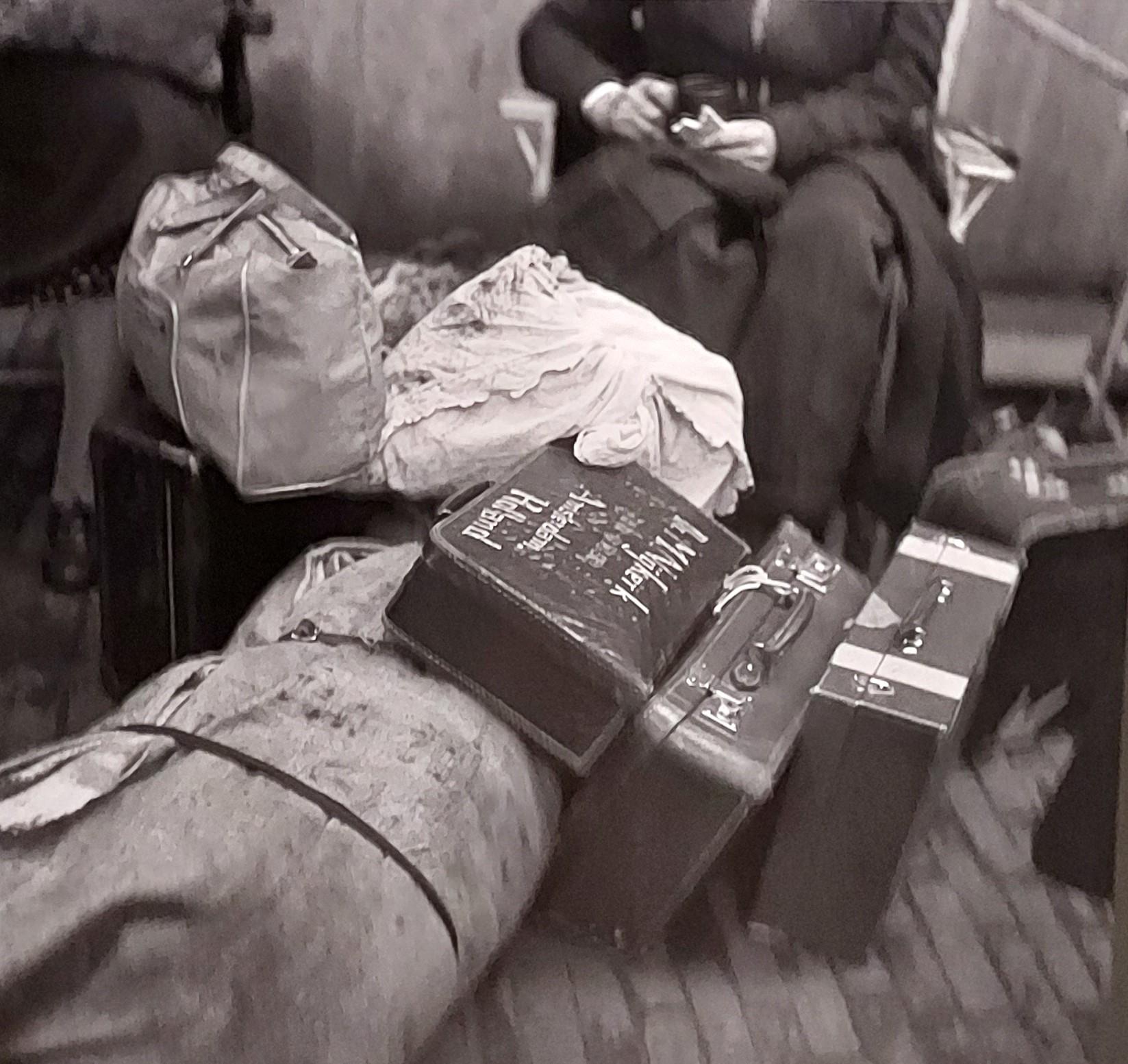Zwart wit foto van Maria Austria 'Joden keren terug uit Westerbork'. Op voorgrond koffertjes, tassen en een plunjezak. Op achtergrond zijn de eigenaren vaag en gedeeltelijk zichtbaar