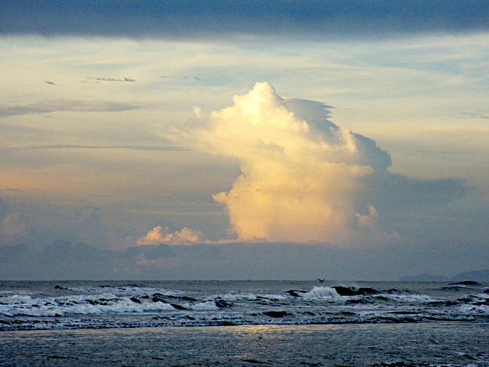 Foto van zee met branding onder door de zon beschenen wolk tussen twee grijze wolkenlagen
