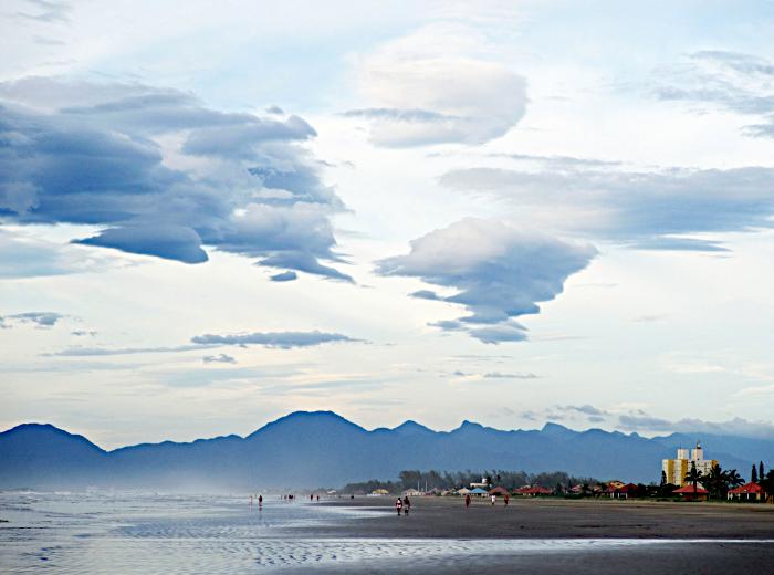 Foto van strand met enkele wandelaars en bergen onder een aantal wolken