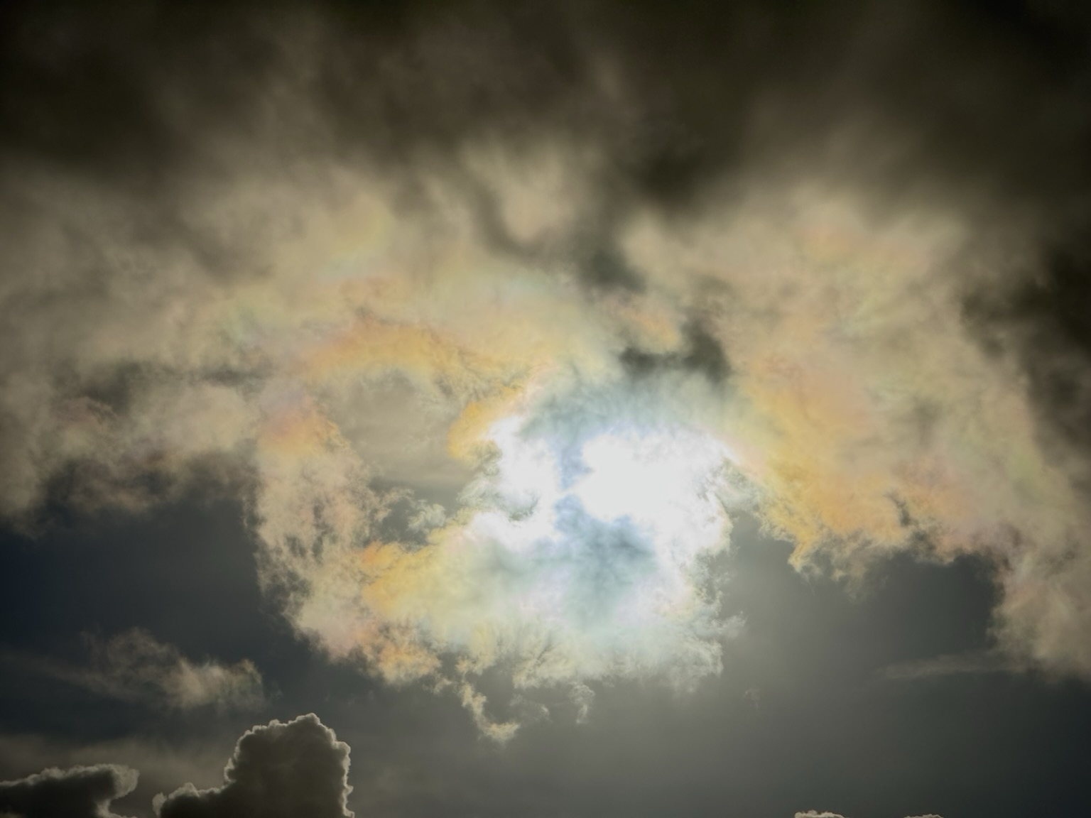 The sun shining through a layer of clouds, fracturing the light into rainbow colours. Epic, colourful and ethereal looking sky photograph.